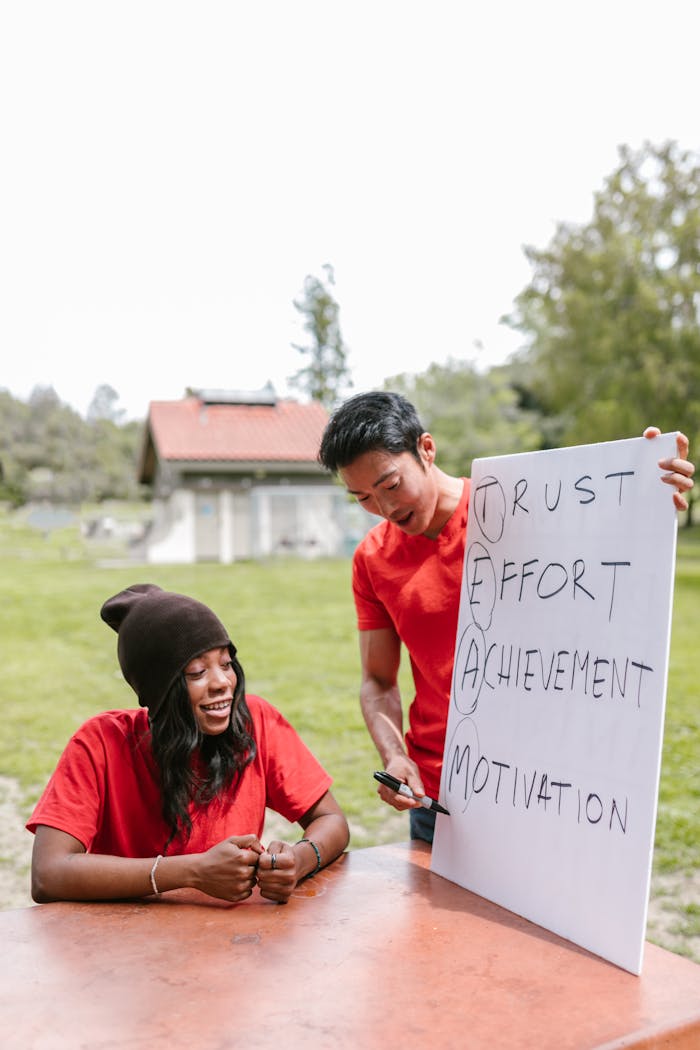 Two adults engaging in an outdoor team building activity with a motivational sign, showing teamwork and collaboration.